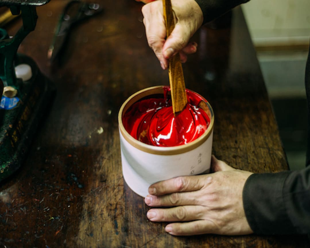 An artist working red pigment into urushi lacquer